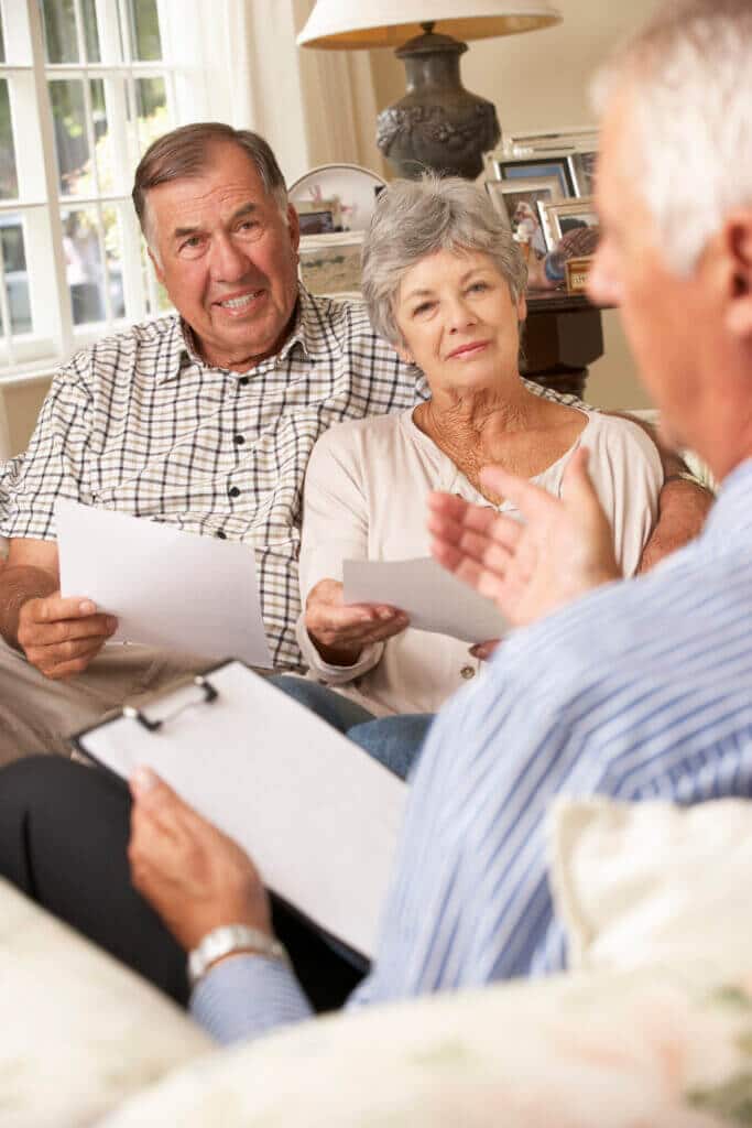 Retired Senior Couple Sitting On Sofa Talking To Financial Advisor